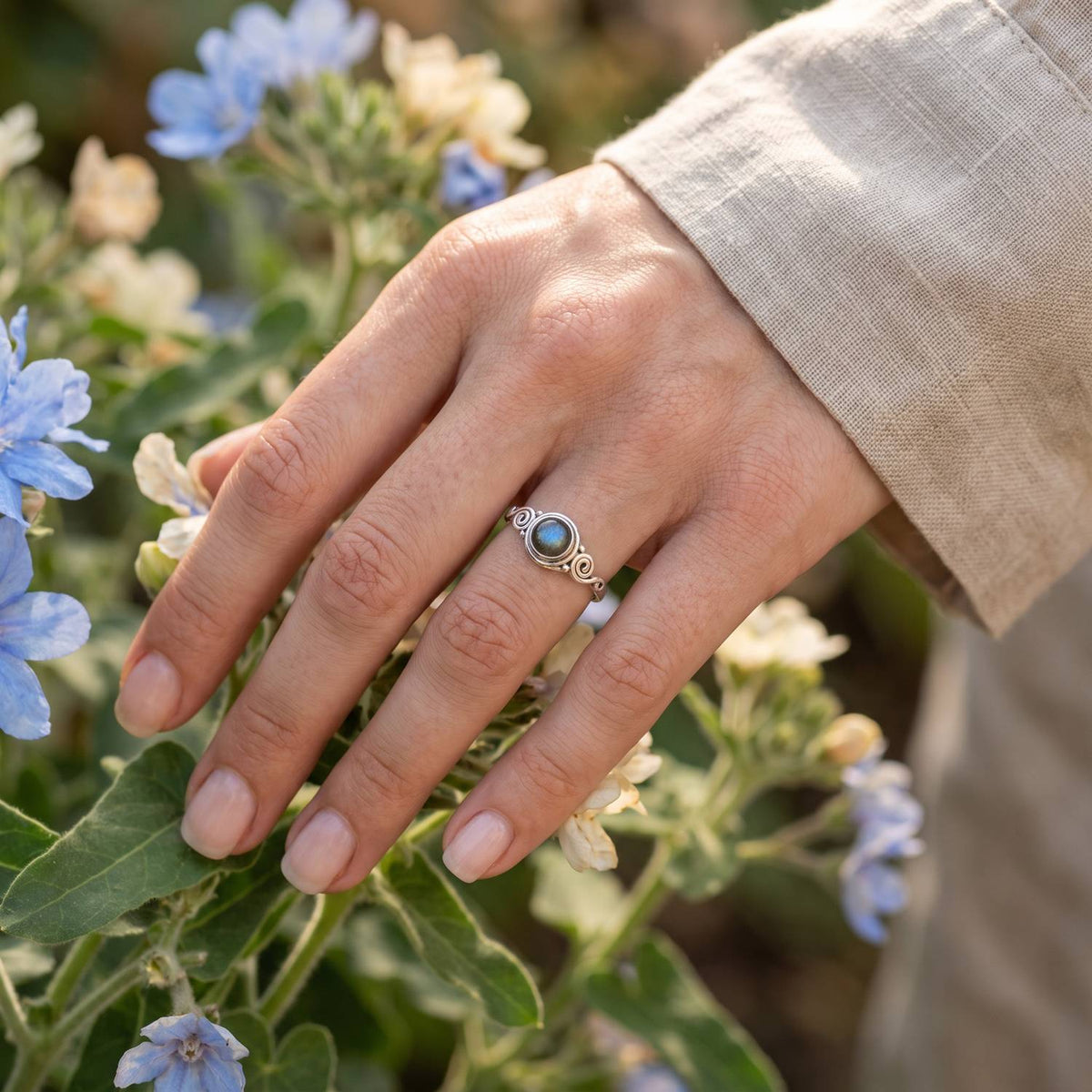 Silberring mit Labradorit an der Hand zwischen Blumen