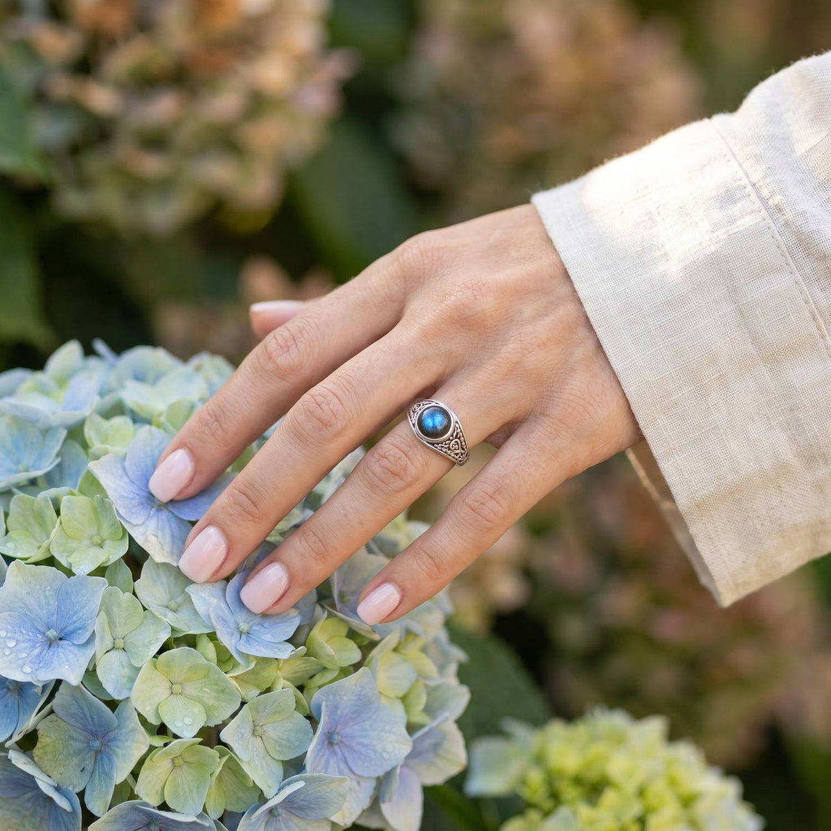 Silberring mit Labradorit an der Hand zwischen Blumen