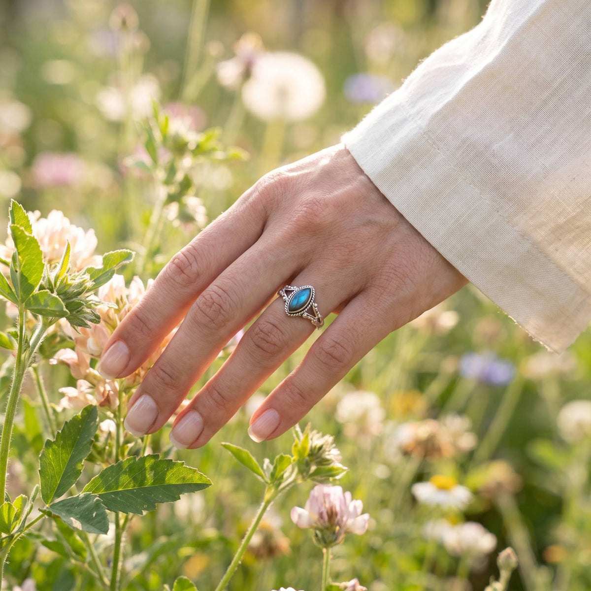 Silberring mit Labradorit an der Hand zwischen Blumen