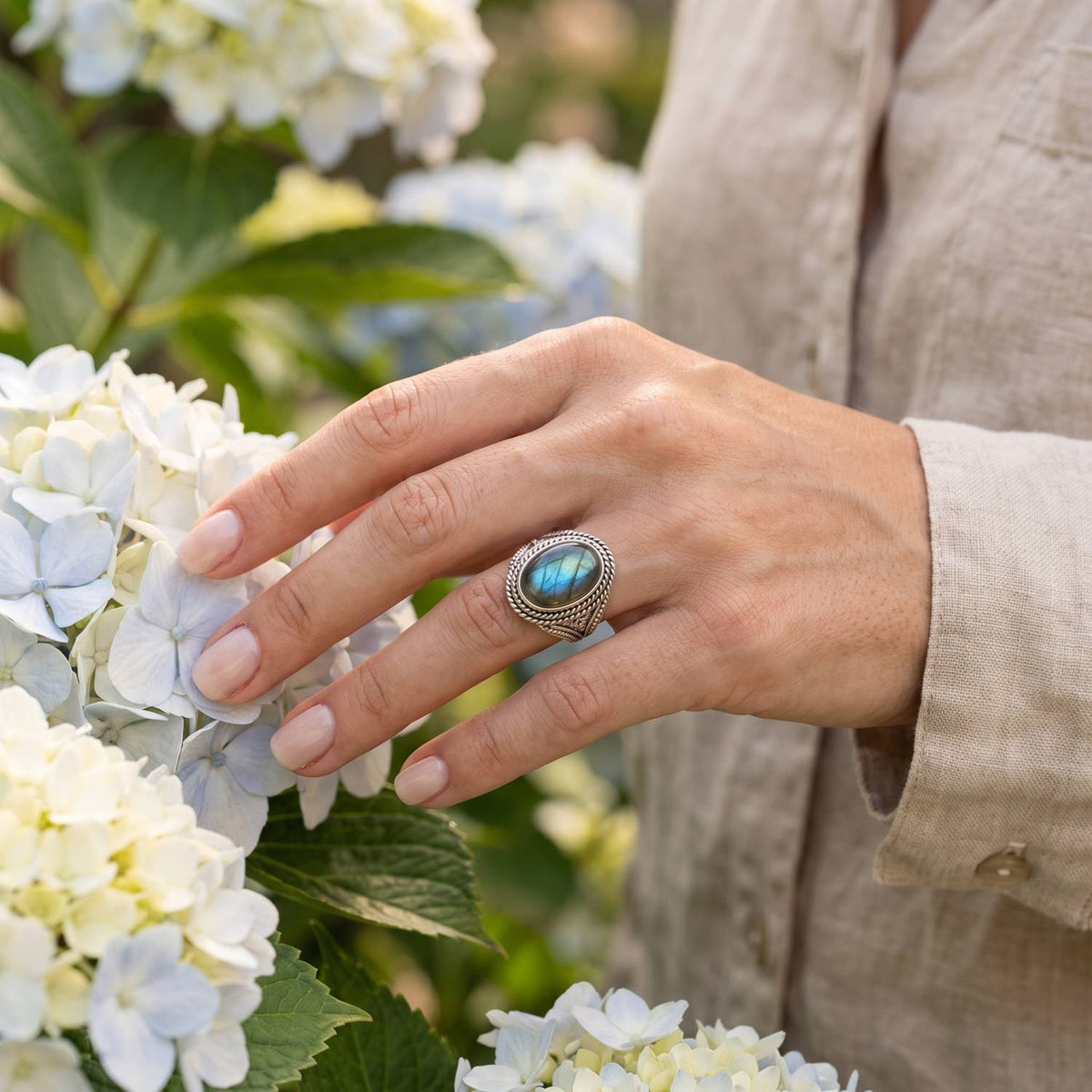 Silberring mit Labradorit an der Hand zwischen Blumen