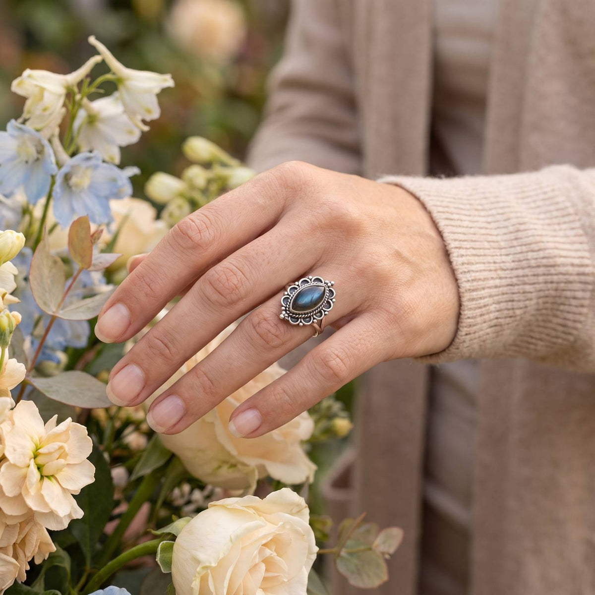 Silberring mit Labradorit an der Hand zwischen Blumen
