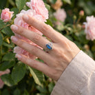[KI] Silberring mit Labradorit an der Hand zwischen Blumen