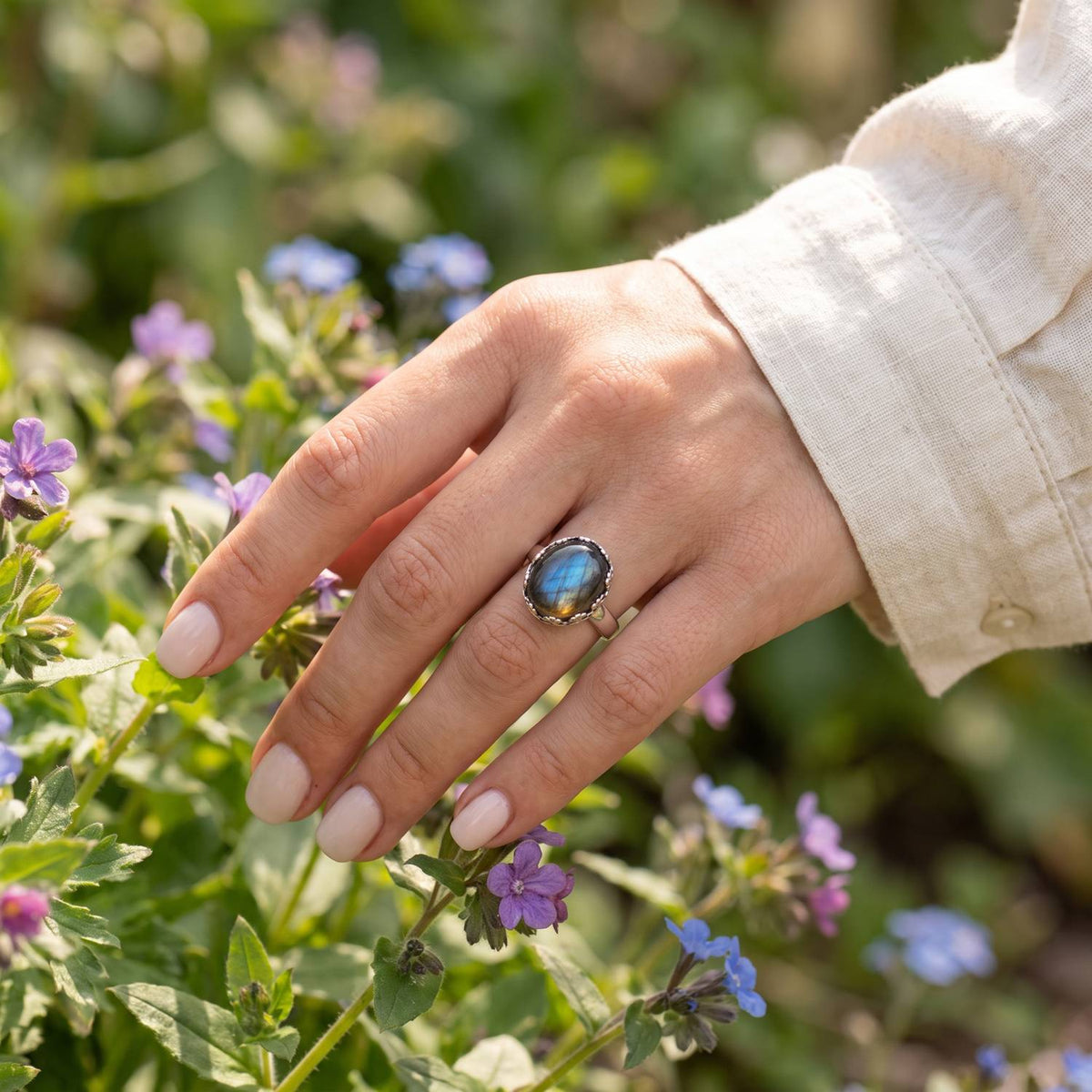 Silberring mit Labradorit an der Hand zwischen Blumen