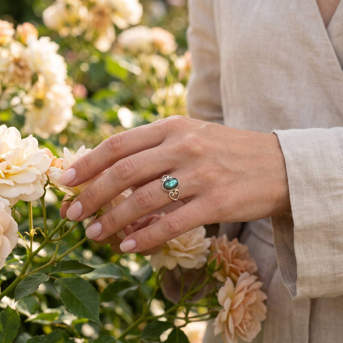Silberring mit Labradorit an der Hand zwischen Blumen