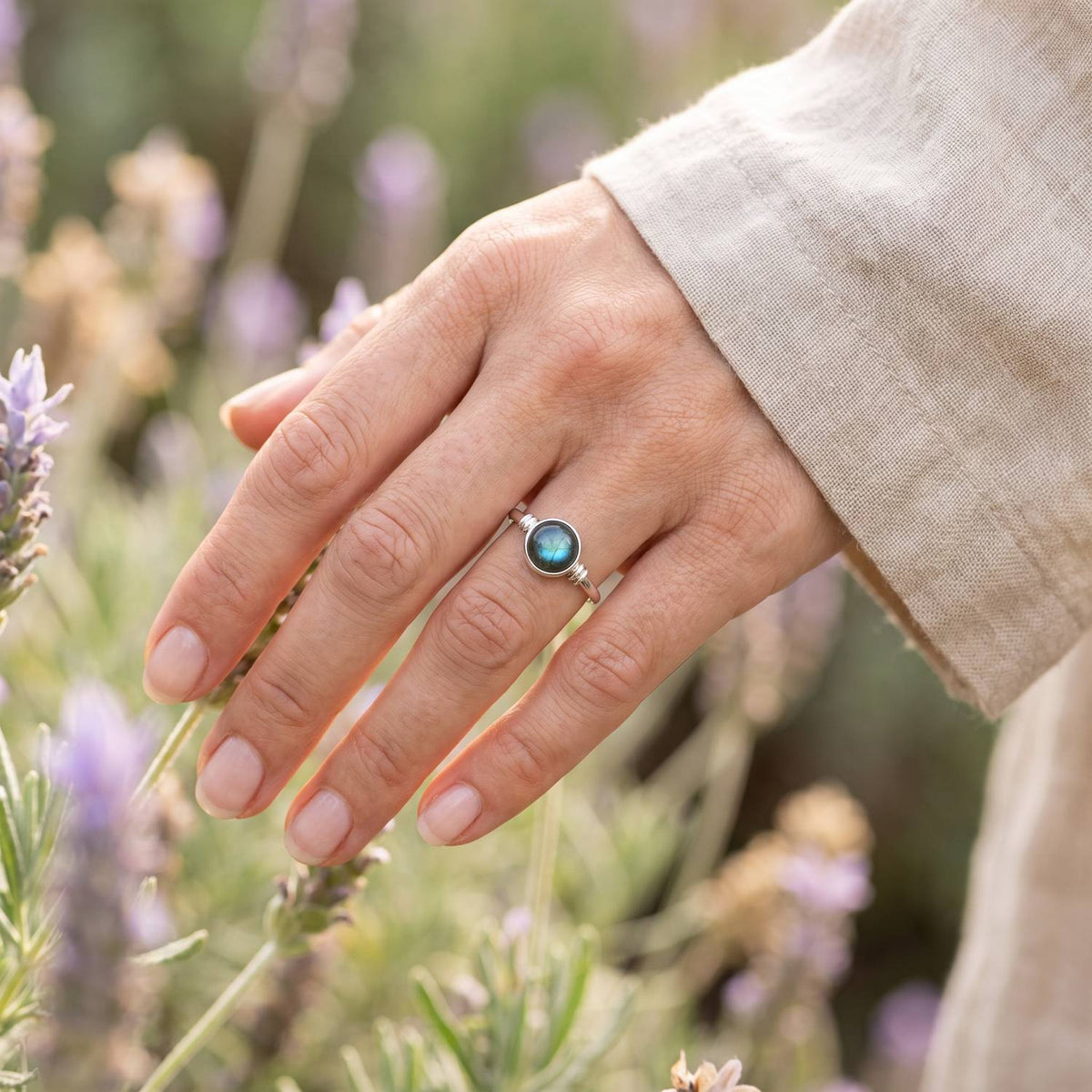 Silberring mit Labradorit an der Hand zwischen Blumen