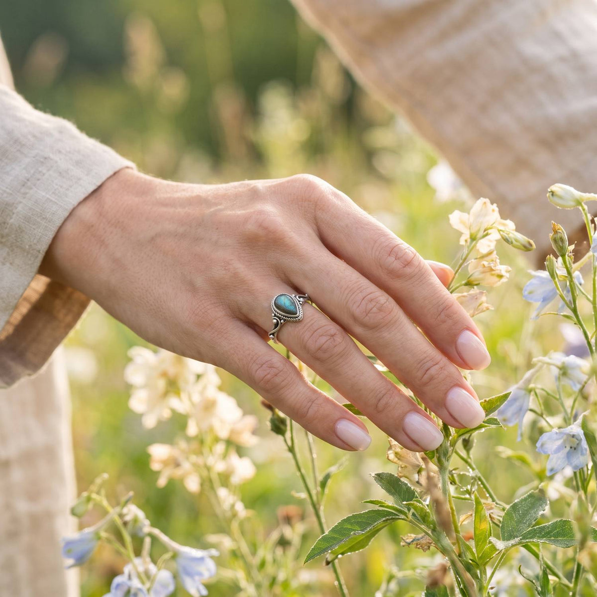 Silberring mit Labradorit an der Hand zwischen Blumen