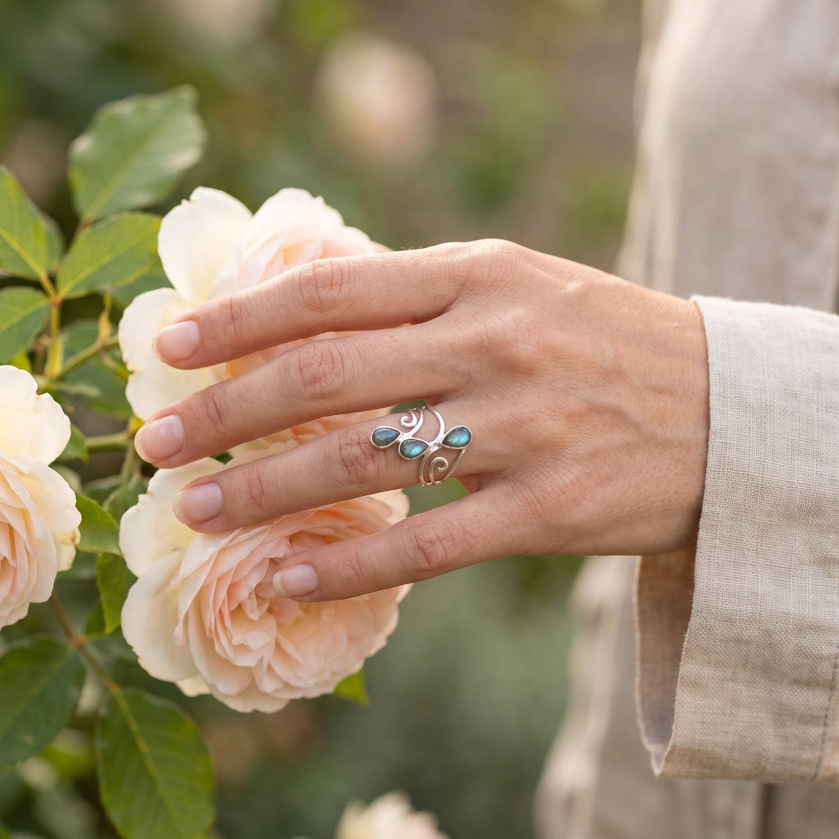 Silberring mit Labradorit an der Hand zwischen Blumen
