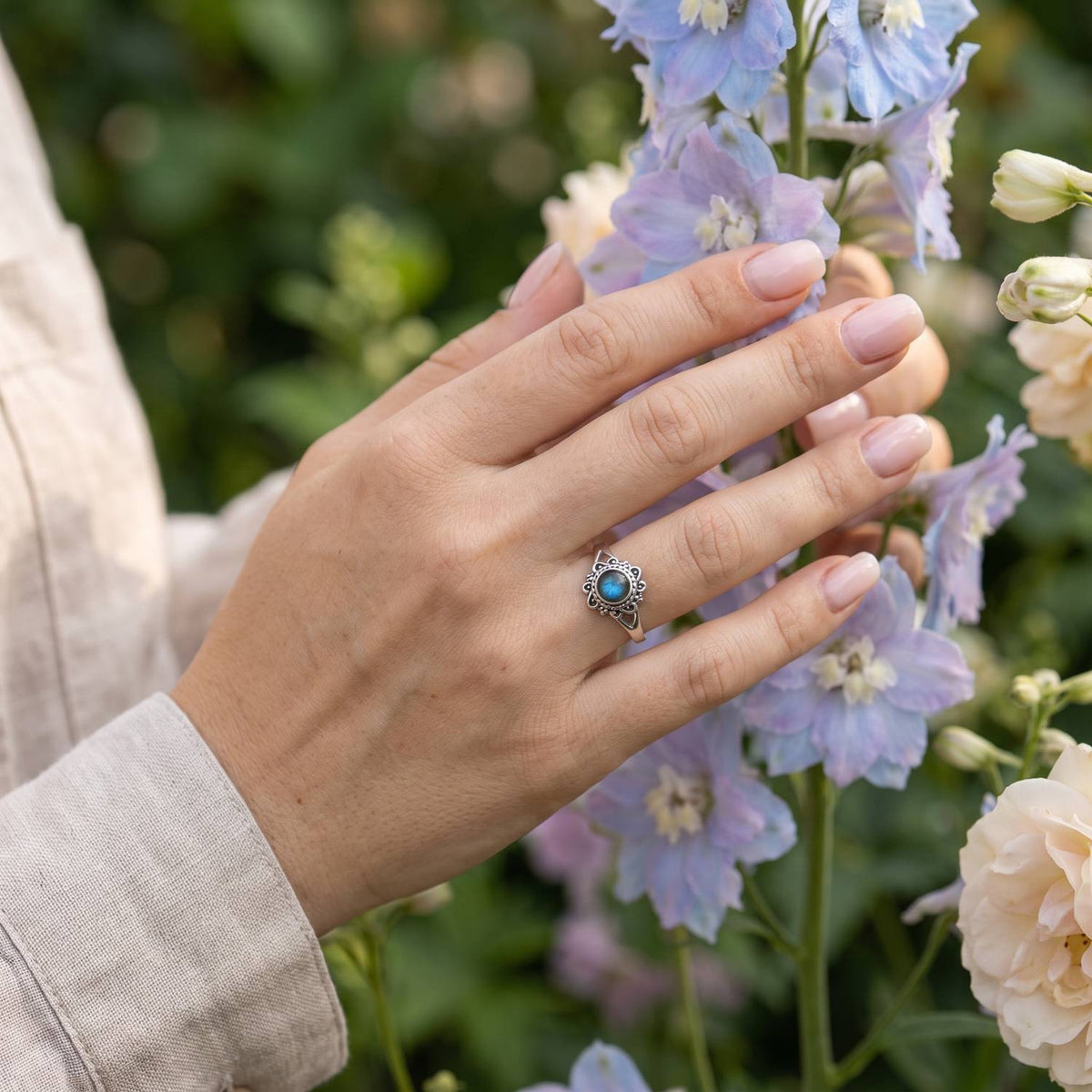 Silberring mit Labradorit an der Hand zwischen Blumen