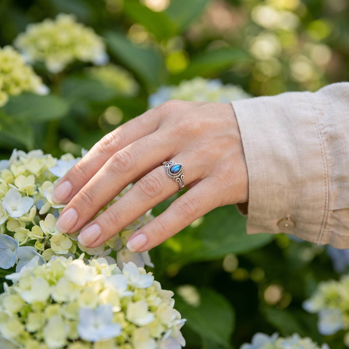 Silberring mit Labradorit an der Hand zwischen Blumen