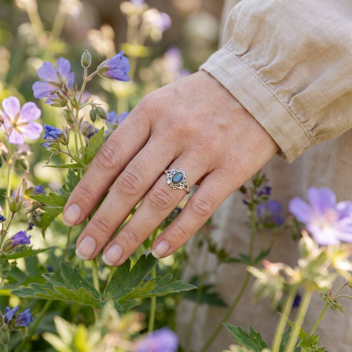 Silberring mit Labradorit an der Hand zwischen Blumen