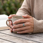 [KI] Labradoritring aus Silber getragen beim Lesen mit einer Tasse