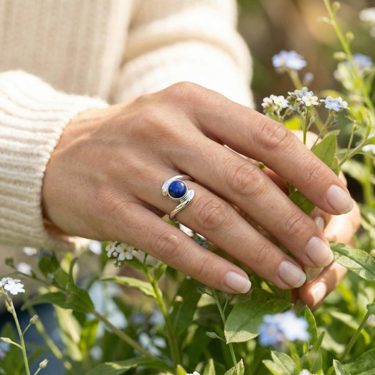 Silberring mit Lapislazuli an der Hand zwischen Blumen