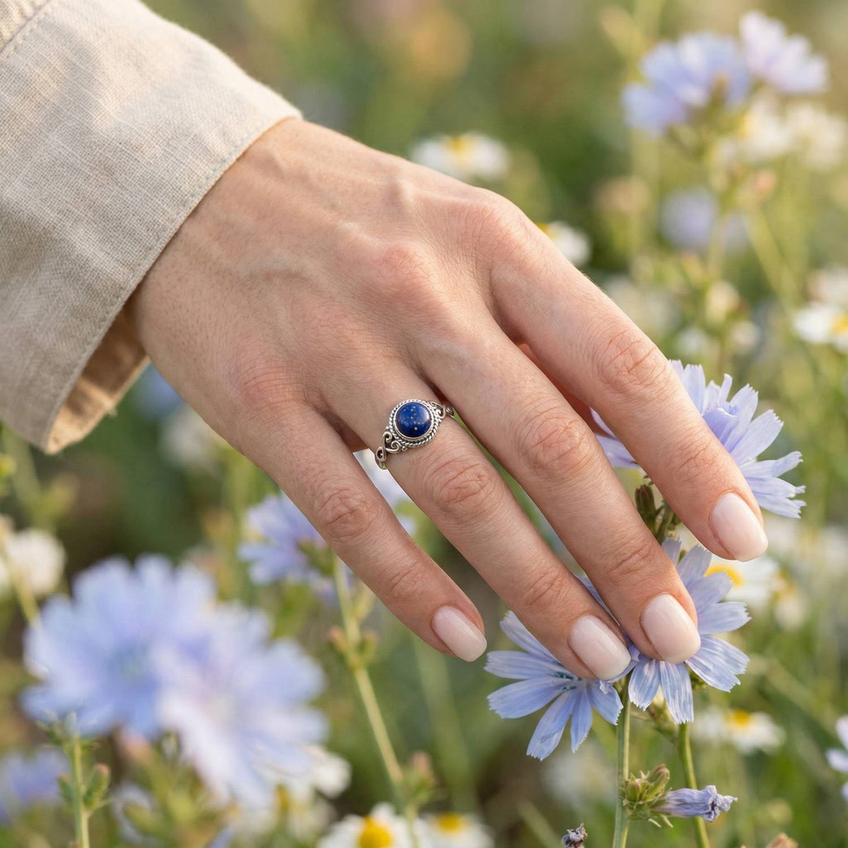 Silberring mit Lapislazuli an der Hand zwischen Blumen