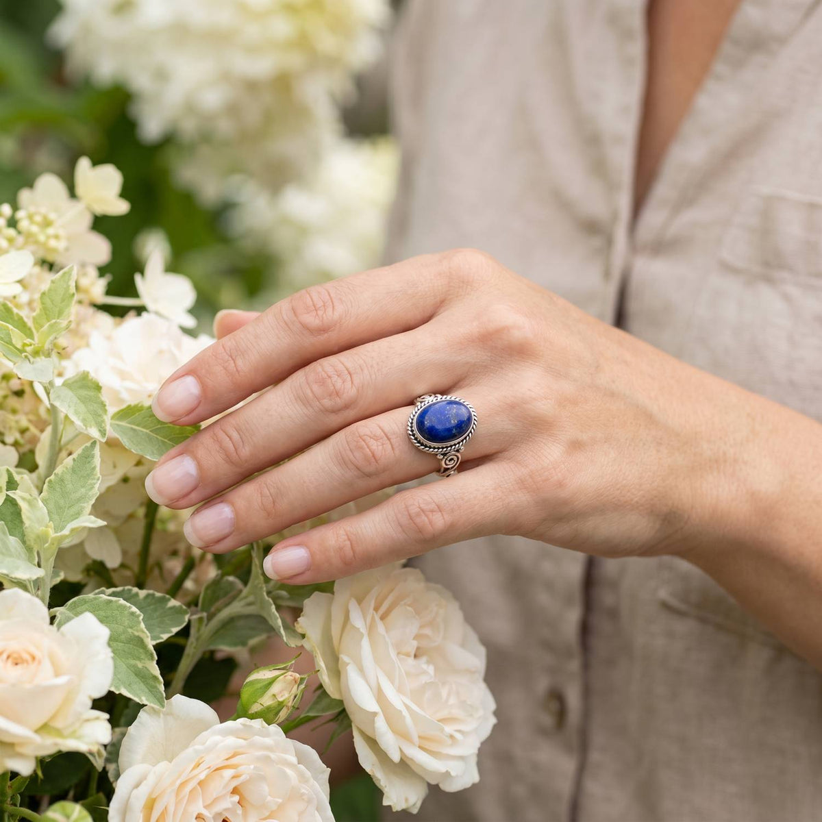 Silberring mit Lapislazuli an der Hand zwischen Blumen
