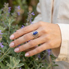 [KI] Silberring mit Lapislazuli an der Hand zwischen Blumen