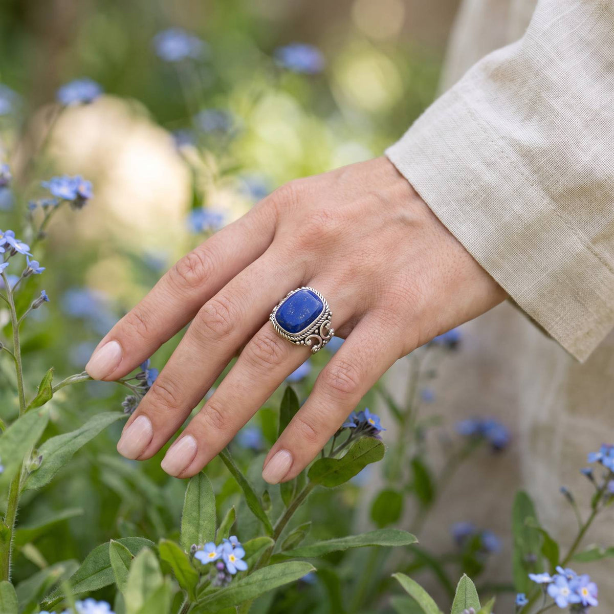 Silberring mit Lapislazuli an der Hand zwischen Blumen