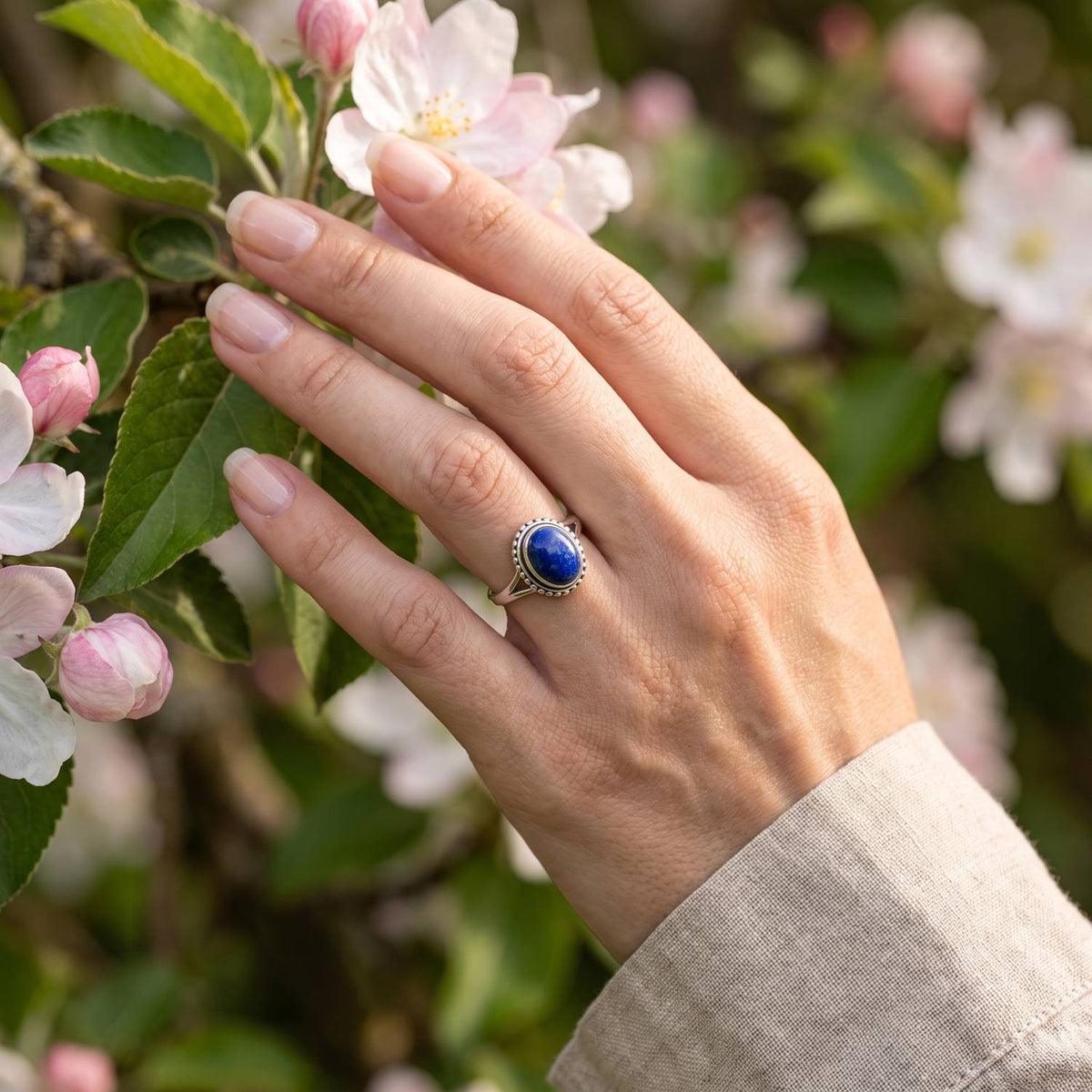 Silberring mit Lapislazuli an der Hand zwischen Blumen