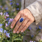 [KI] Silberring mit Lapislazuli an der Hand zwischen Blumen