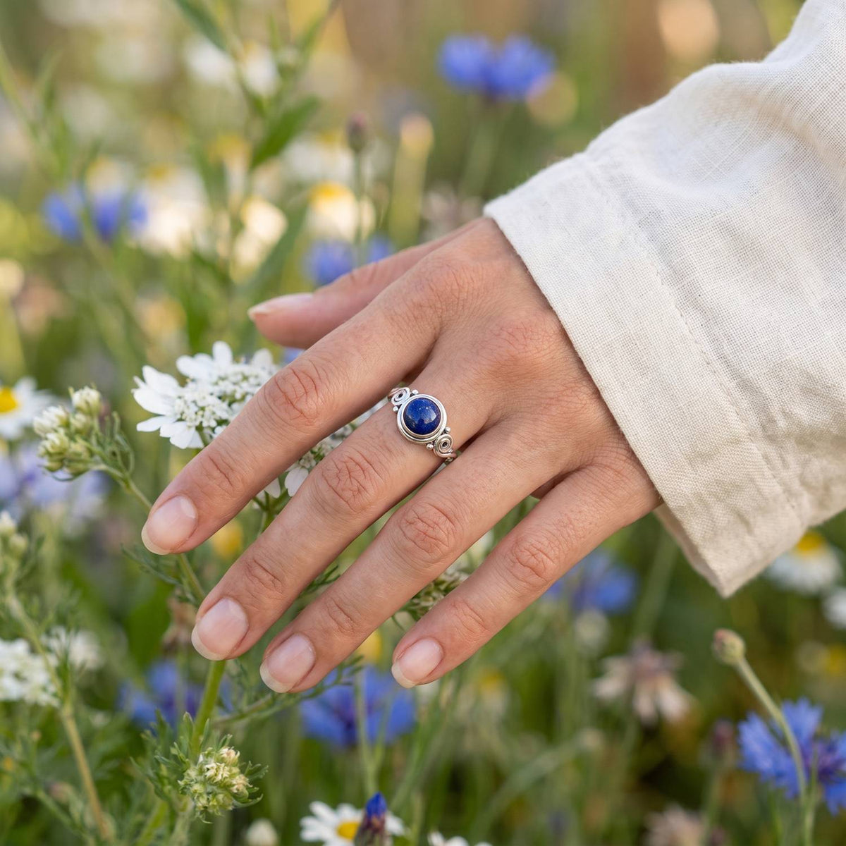Silberring mit Lapislazuli an der Hand zwischen Blumen