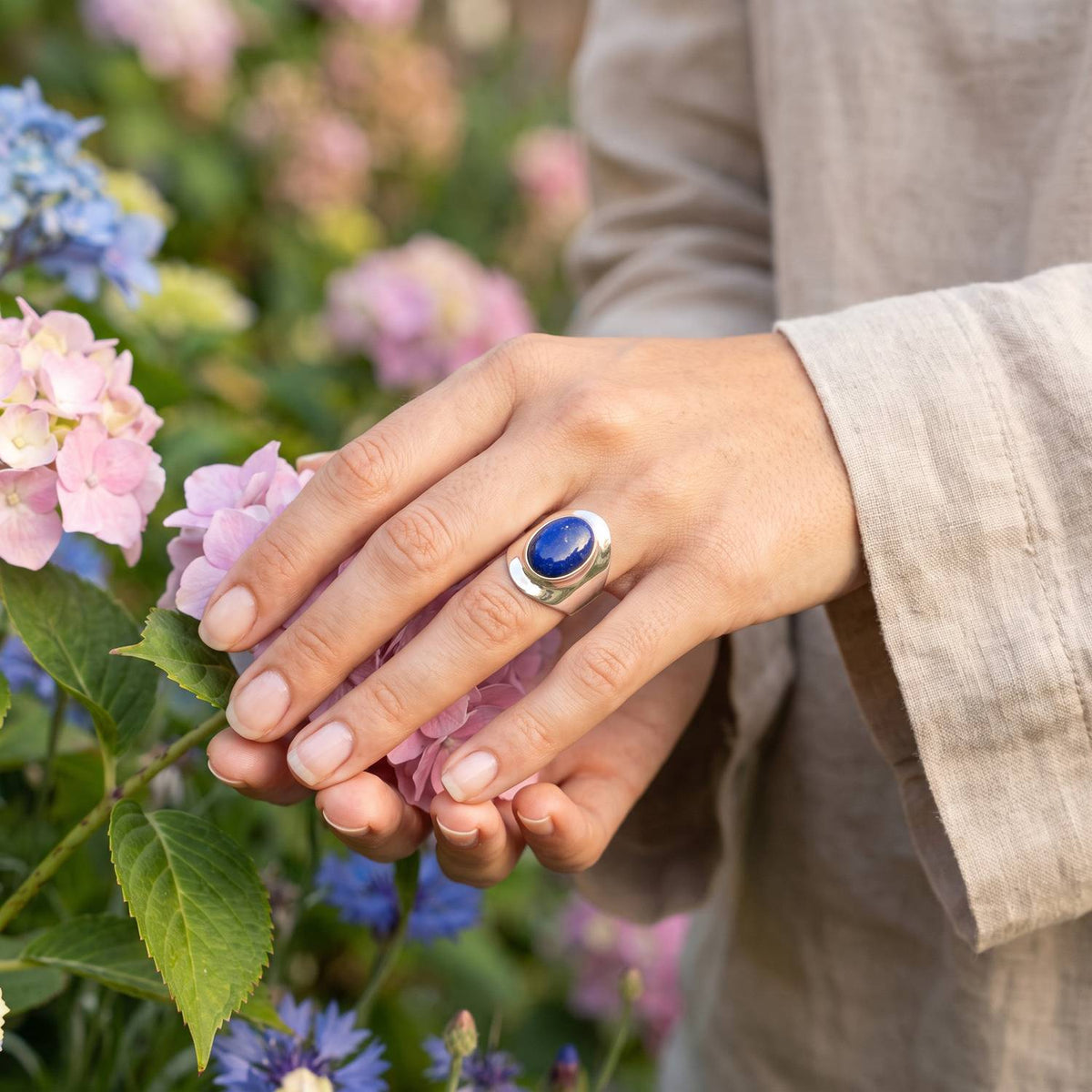 Silberring mit Lapislazuli an der Hand zwischen Blumen