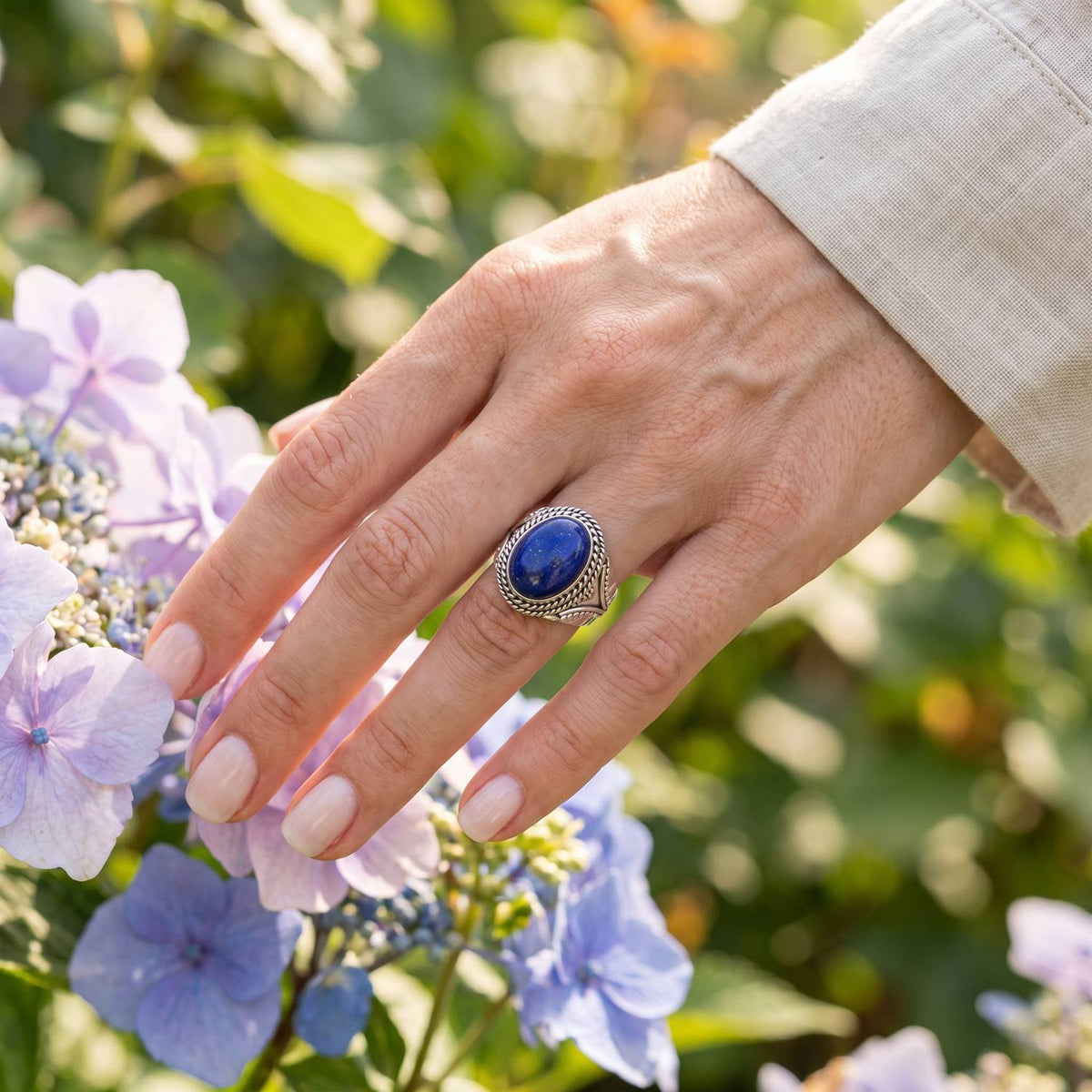 Silberring mit Lapislazuli an der Hand zwischen Blumen
