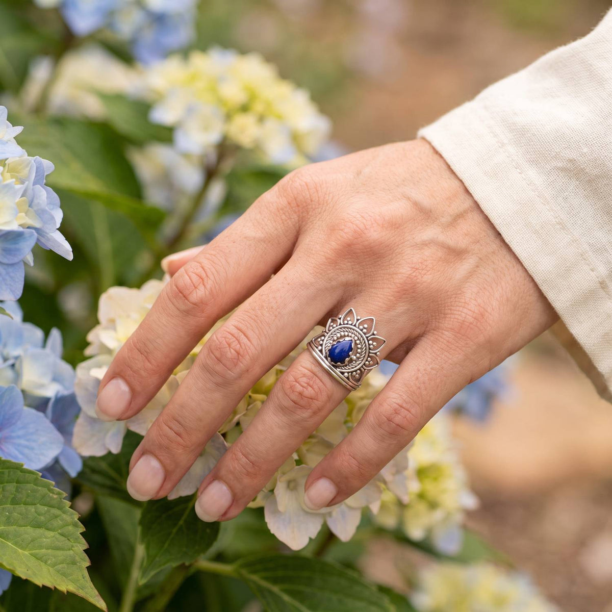 Silberring mit Lapislazuli an der Hand zwischen Blumen