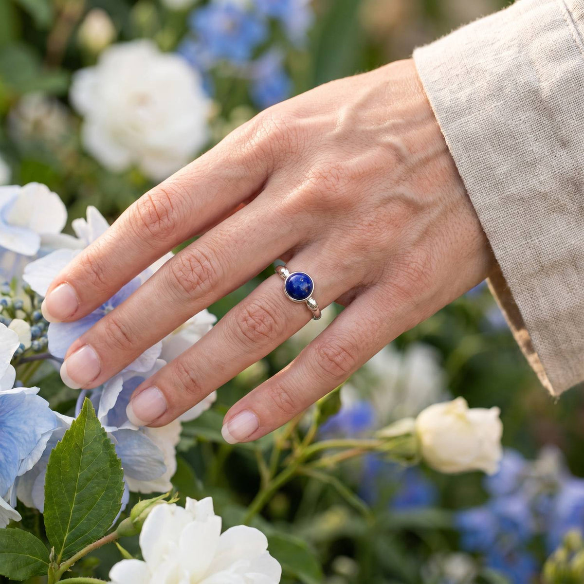 Silberring mit Lapislazuli an der Hand zwischen Blumen