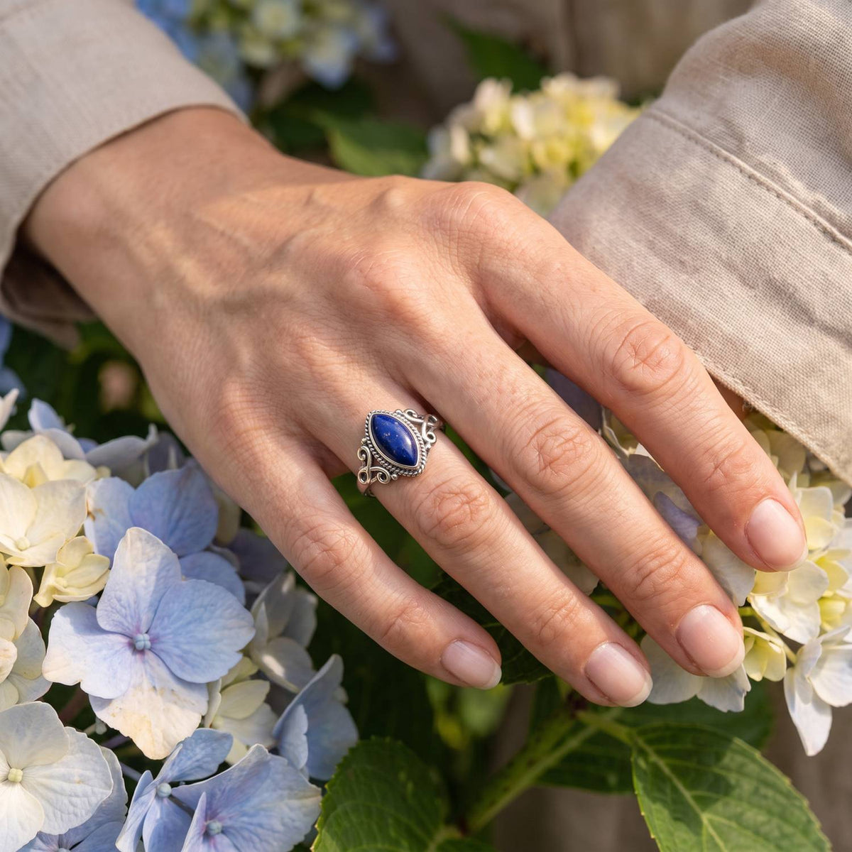 Silberring mit Lapislazuli an der Hand zwischen Blumen