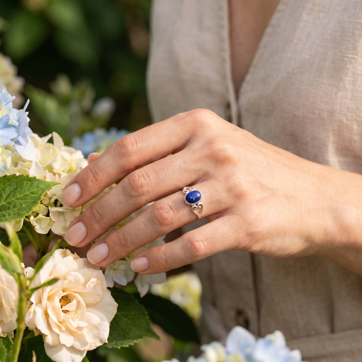 Silberring mit Lapislazuli an der Hand zwischen Blumen