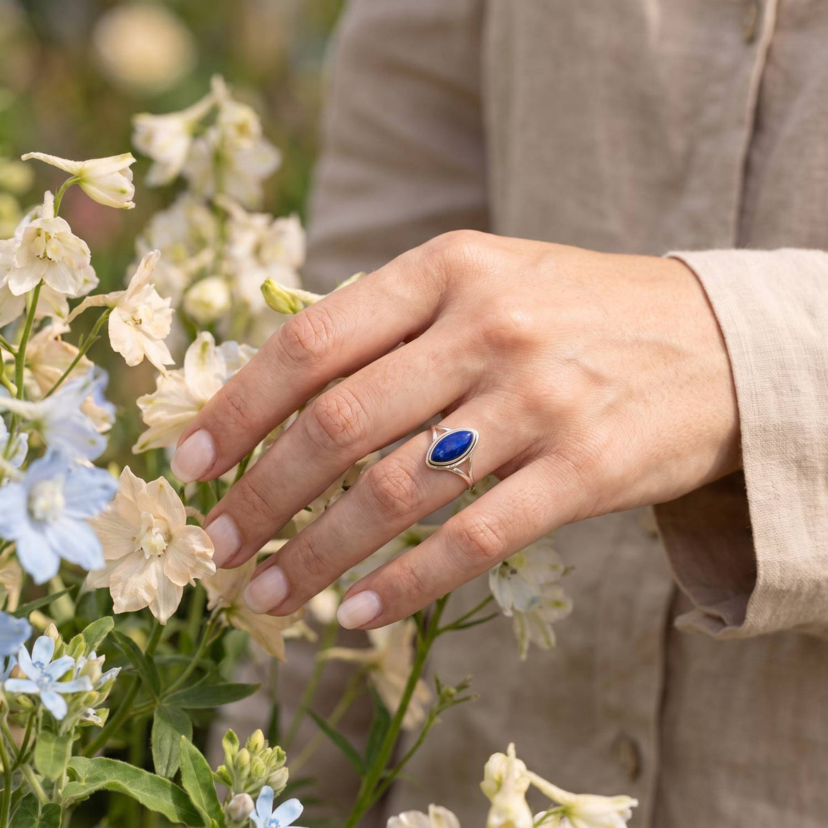 Silberring mit Lapislazuli an der Hand zwischen Blumen