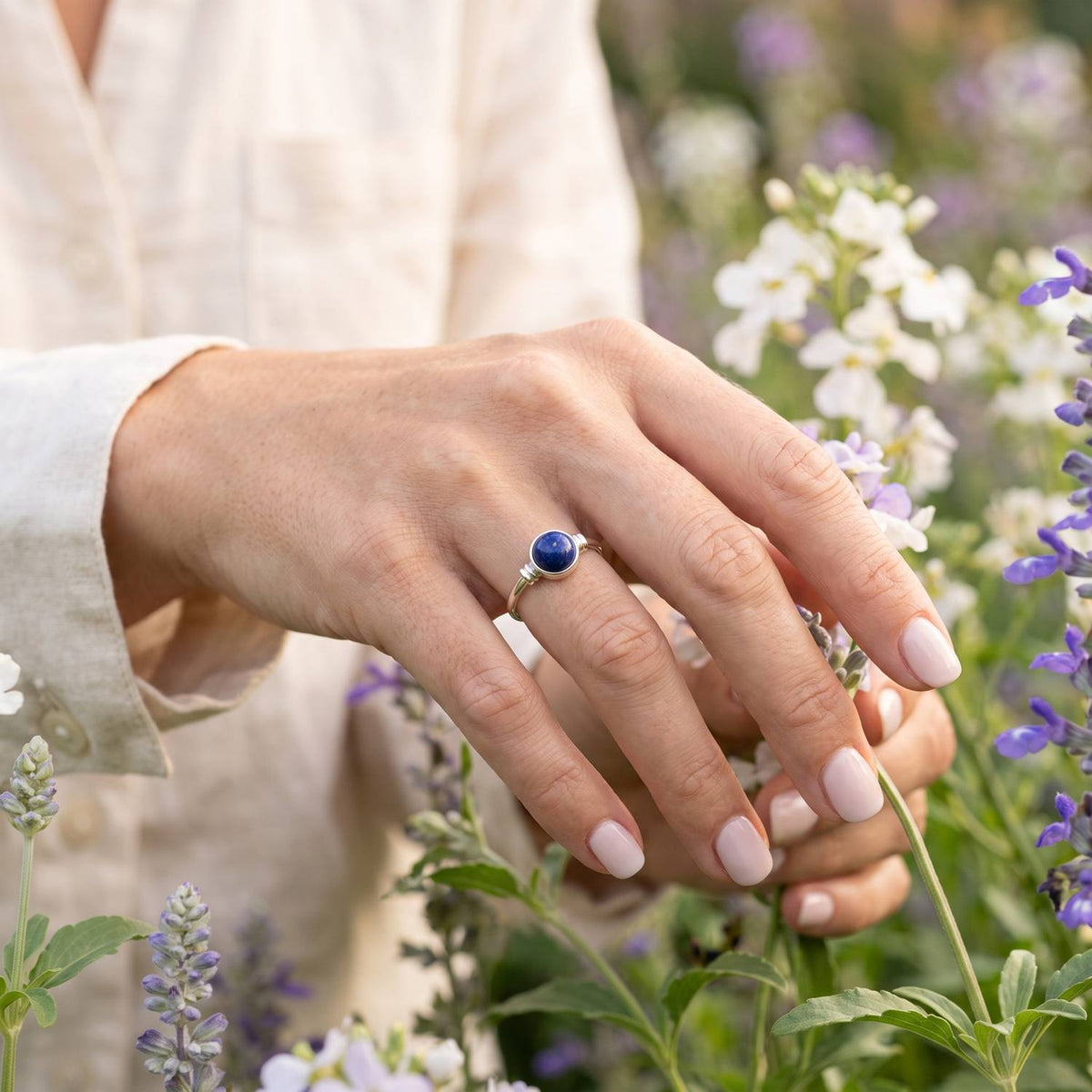 Silberring mit Lapislazuli an der Hand zwischen Blumen