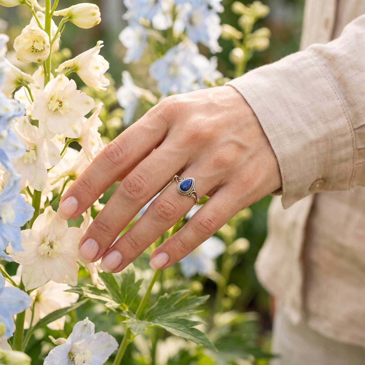 Silberring mit Lapislazuli an der Hand zwischen Blumen