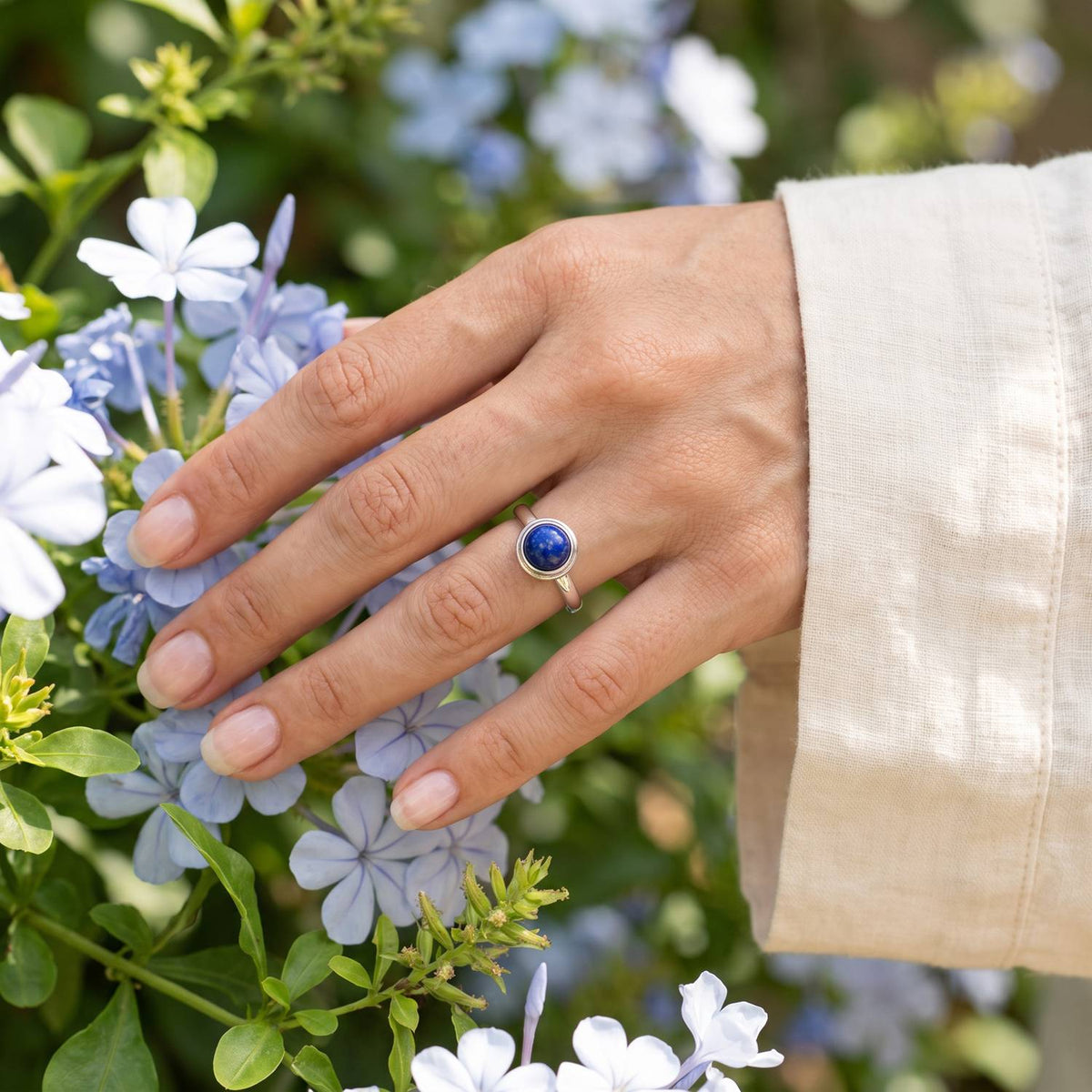 Silberring mit Lapislazuli an der Hand zwischen Blumen