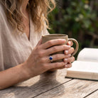 [KI] Lapislazuliring aus Silber getragen beim Lesen mit einer Tasse