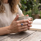 [KI] Lapislazuliring aus Silber getragen beim Lesen mit einer Tasse