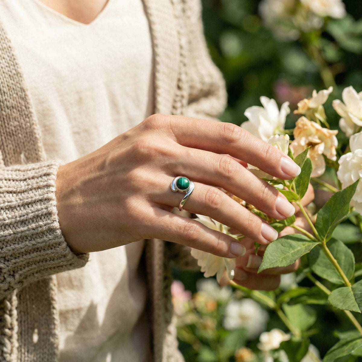 Silberring mit Malachit an der Hand zwischen Blumen