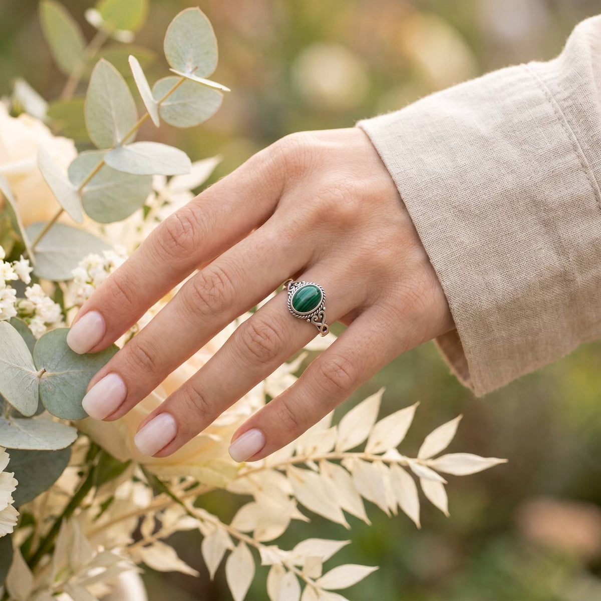 Silberring mit Malachit an der Hand zwischen Blumen