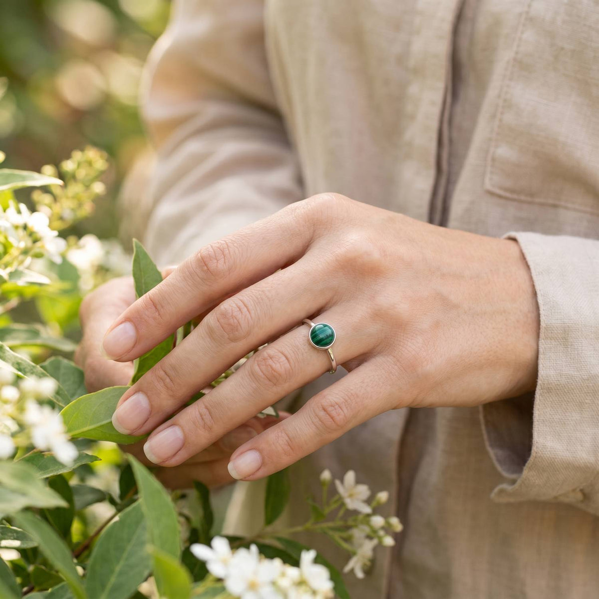 Silberring mit Malachit an der Hand zwischen Blumen