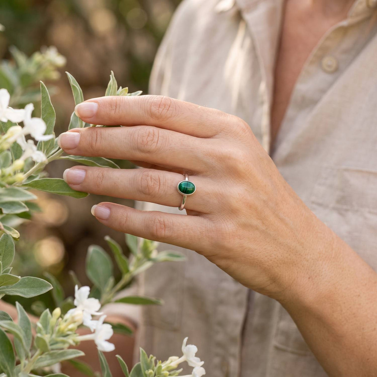 Silberring mit Malachit an der Hand zwischen Blumen