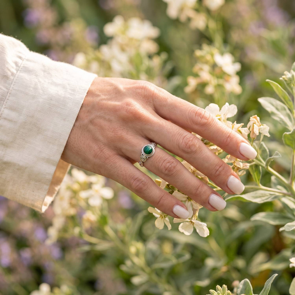 Silberring mit Malachit an der Hand zwischen Blumen