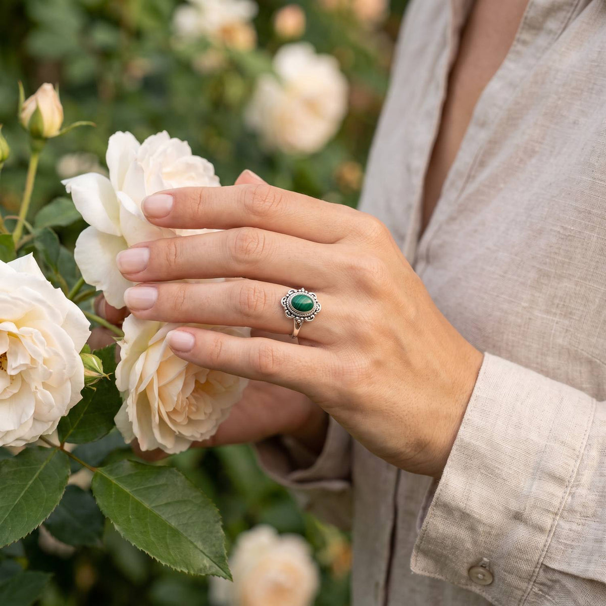 Silberring mit Malachit an der Hand zwischen Blumen