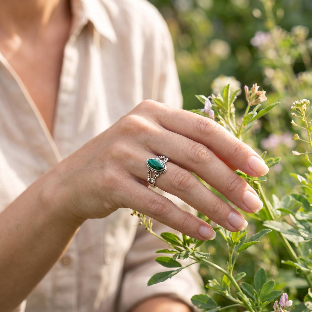Silberring mit Malachit an der Hand zwischen Blumen