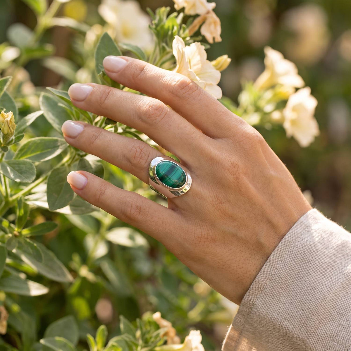 Silberring mit Malachit an der Hand zwischen Blumen