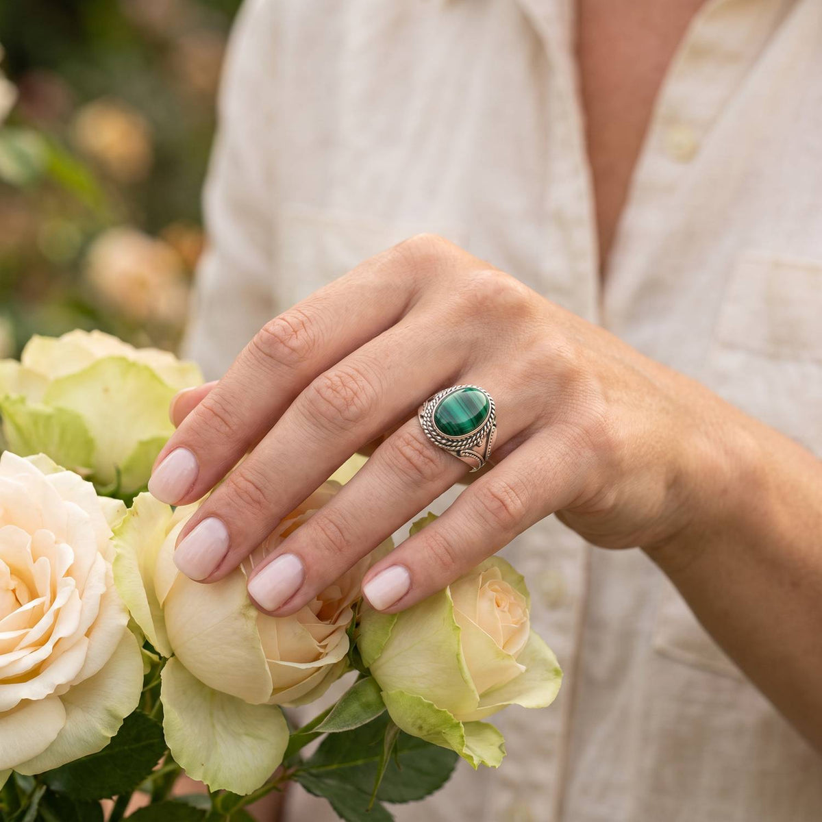 Silberring mit Malachit an der Hand zwischen Blumen