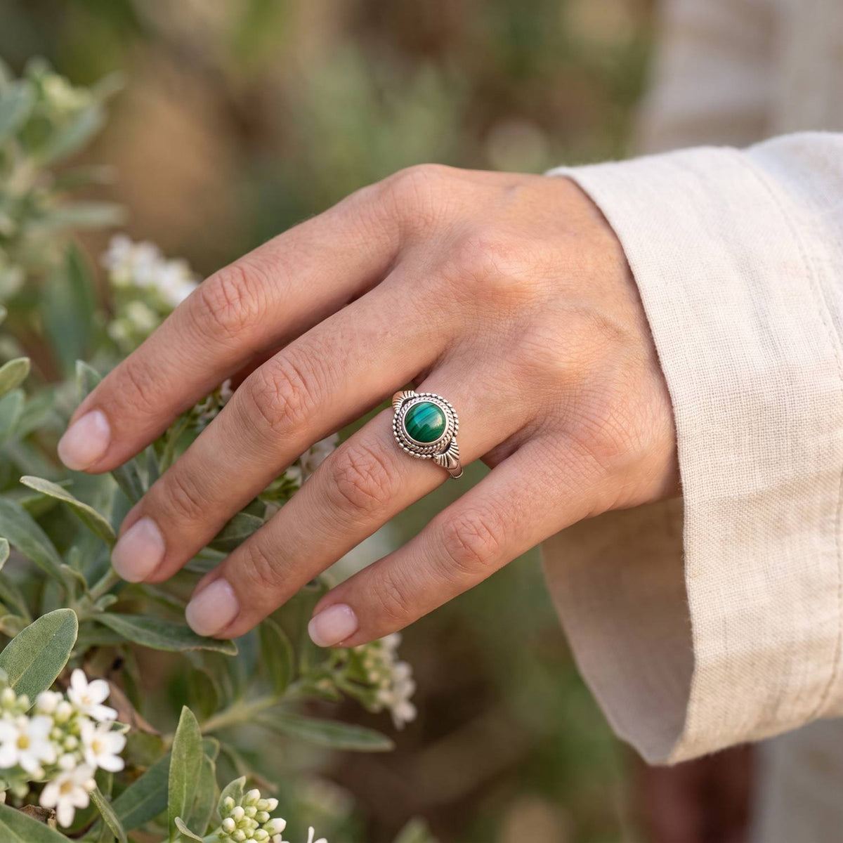 Silberring mit Malachit an der Hand zwischen Blumen