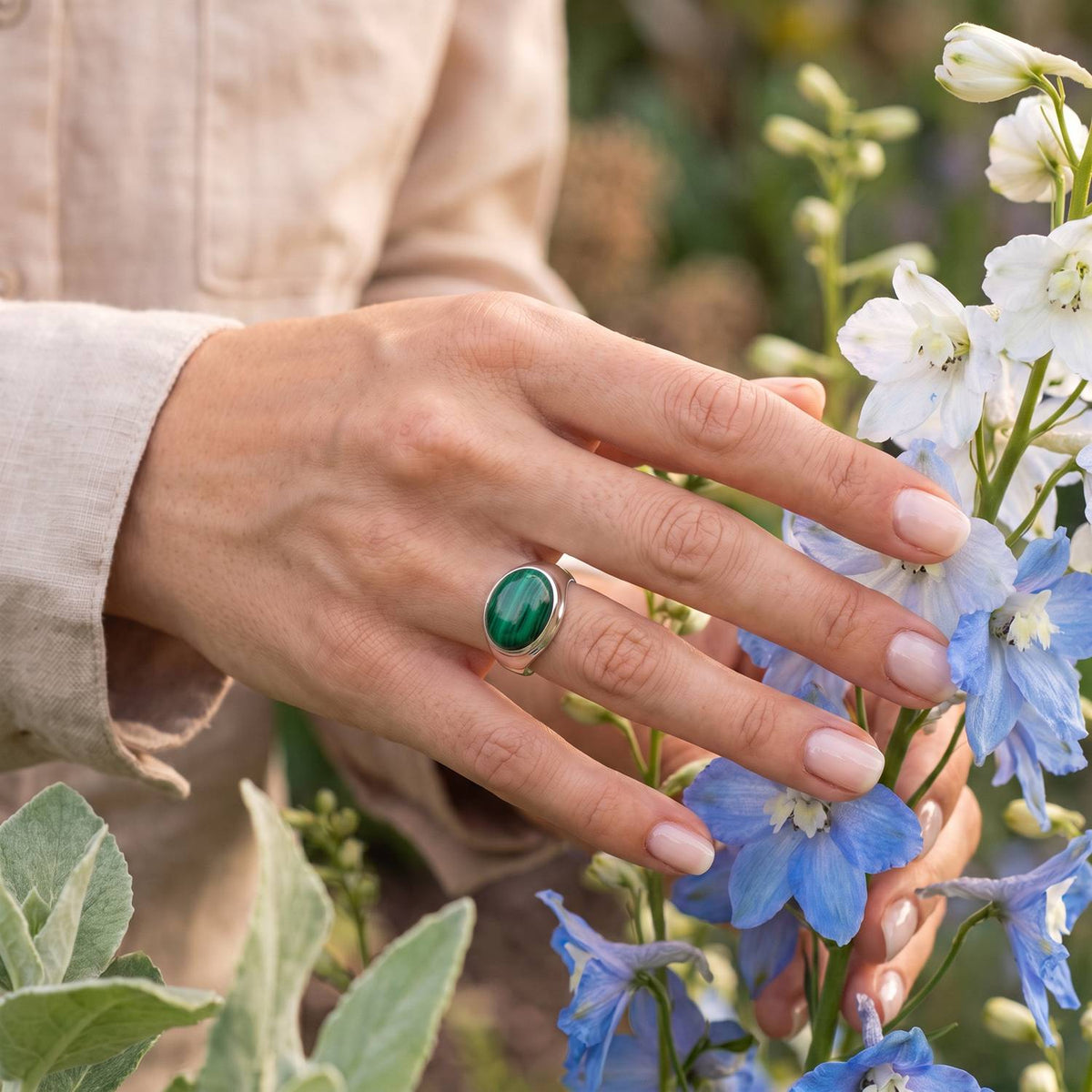 Silberring mit Malachit an der Hand zwischen Blumen