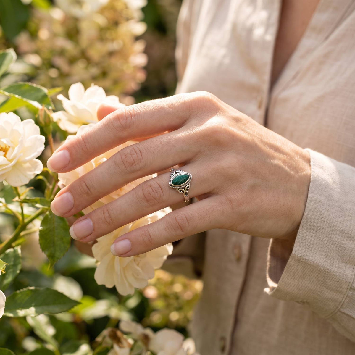 Silberring mit Malachit an der Hand zwischen Blumen