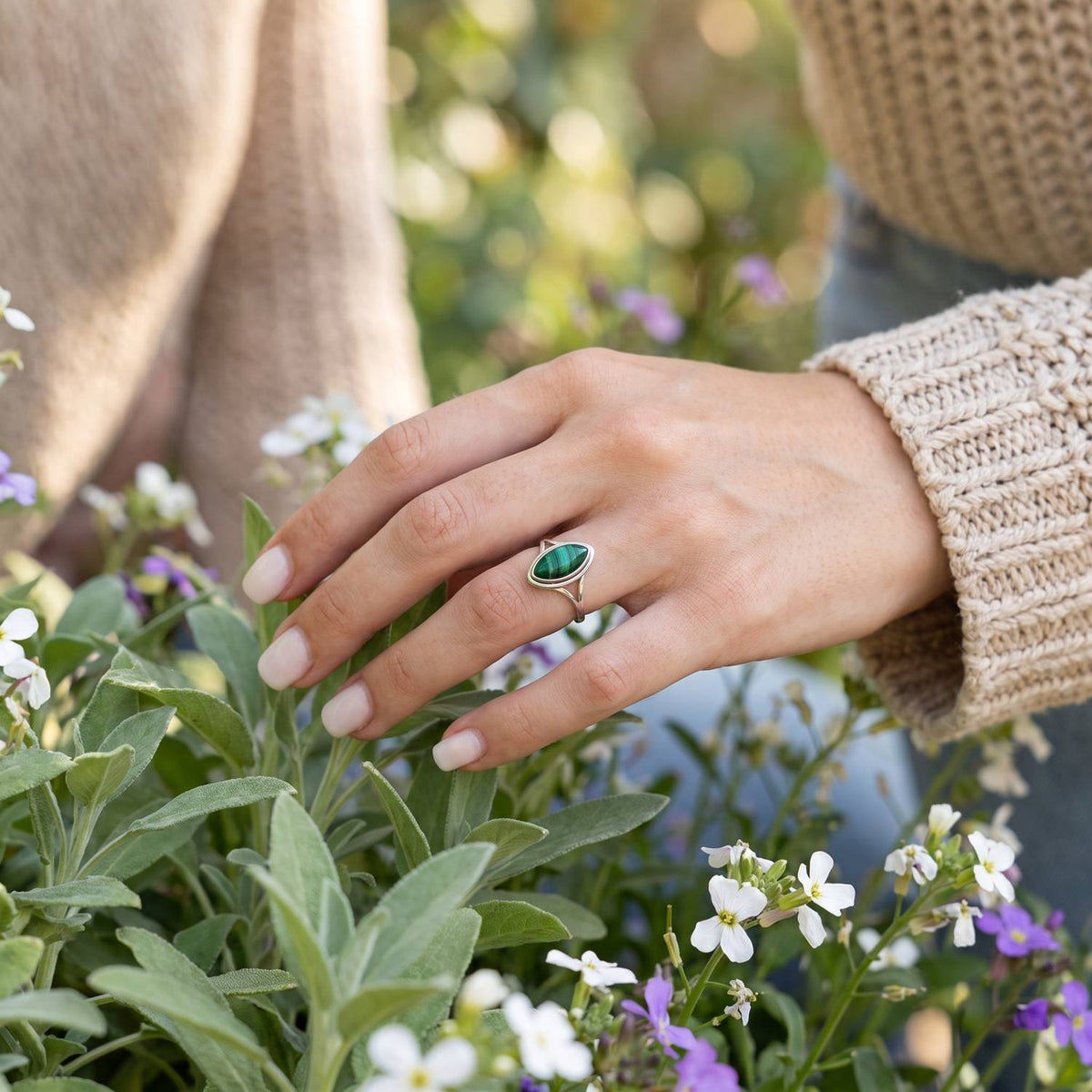 Silberring mit Malachit an der Hand zwischen Blumen