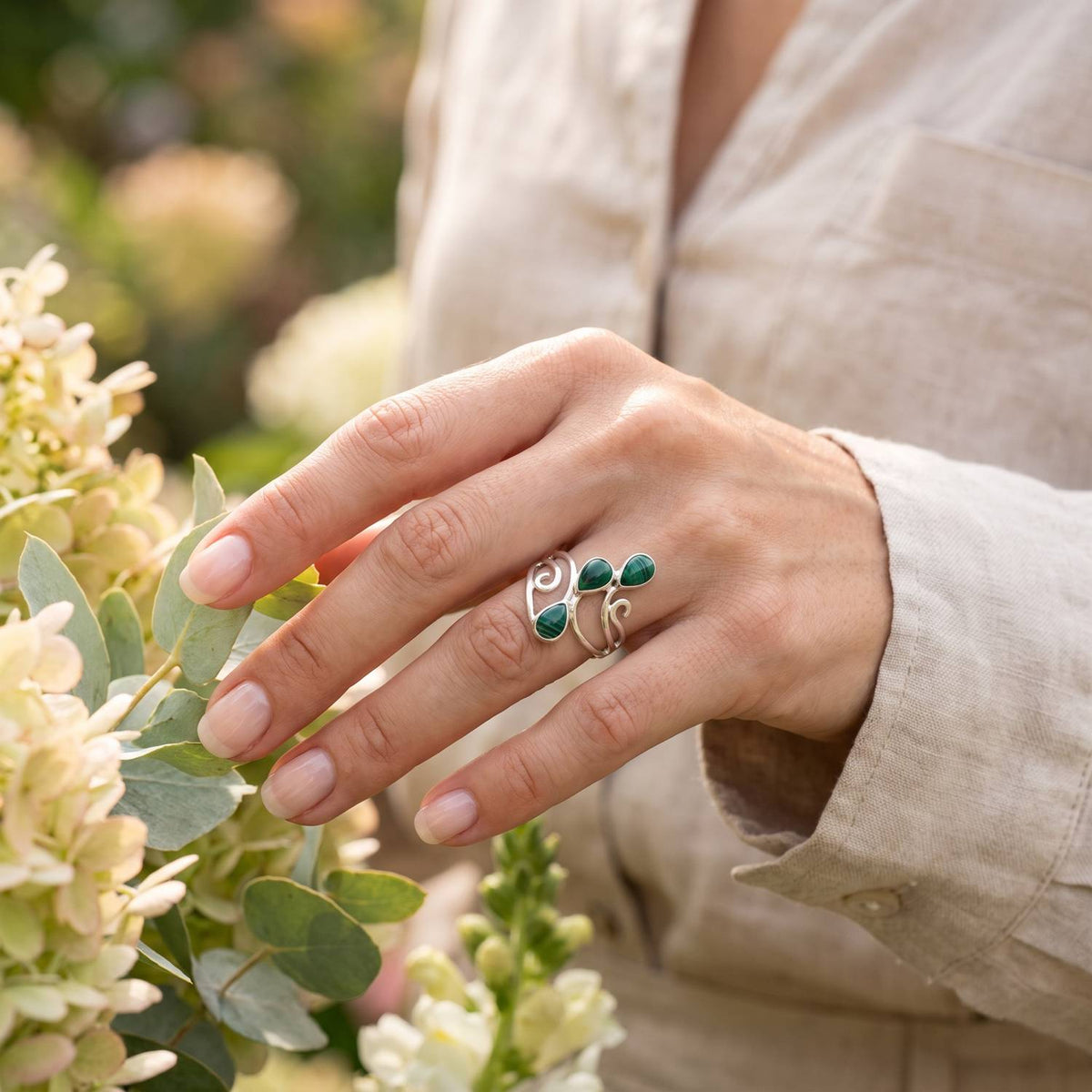 Silberring mit Malachit an der Hand zwischen Blumen