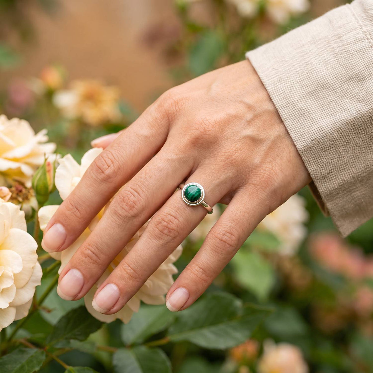 Silberring mit Malachit an der Hand zwischen Blumen